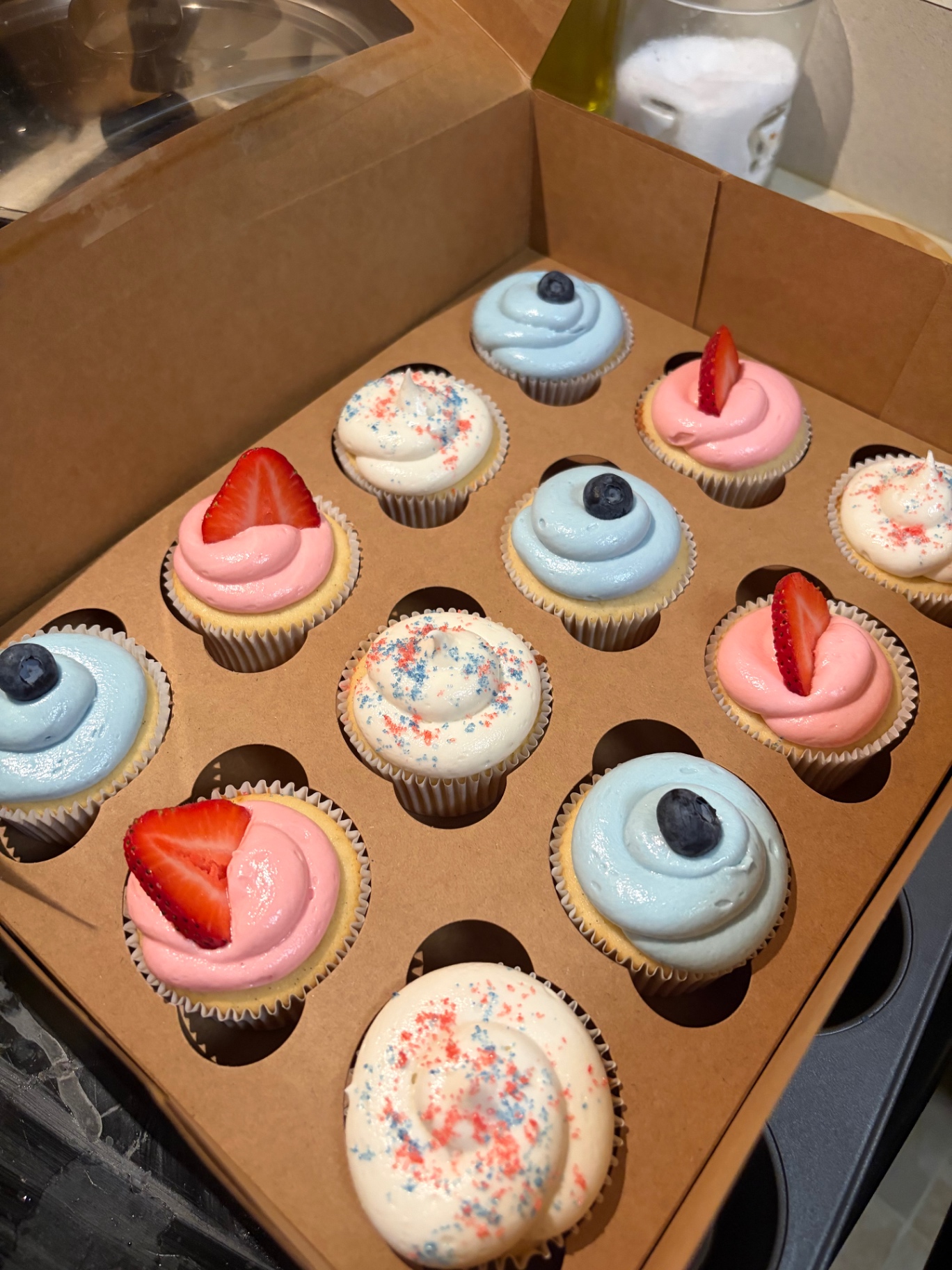 A dozen cupcakes with pink and blue frosting topped with fresh berries